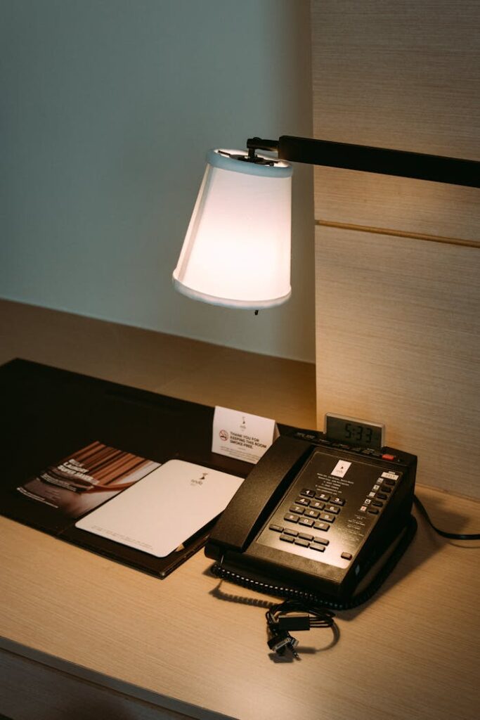 A neatly arranged hotel desk featuring a telephone, lamp, and notebooks in a serene ambiance.